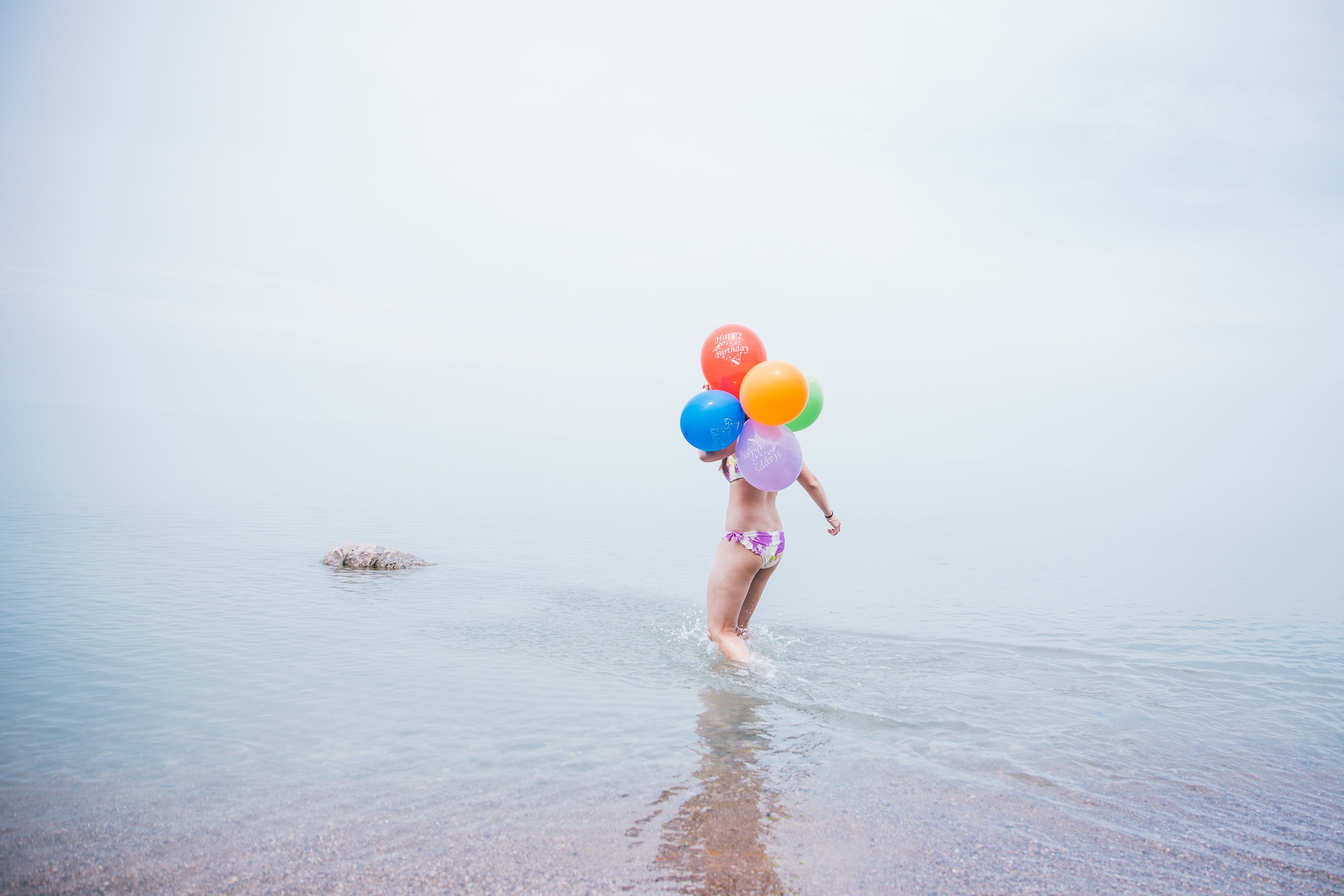 Girl running with helium balloons on the beach